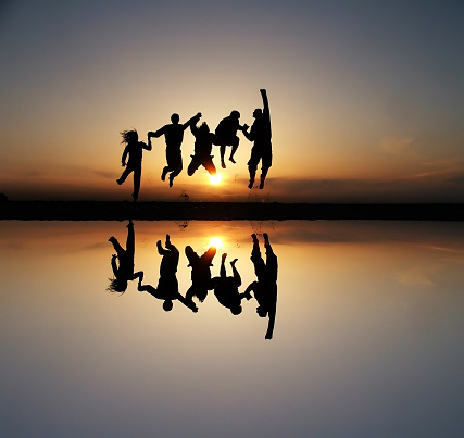 silhouette of friends jumping in sunset at beach with reflection in water
