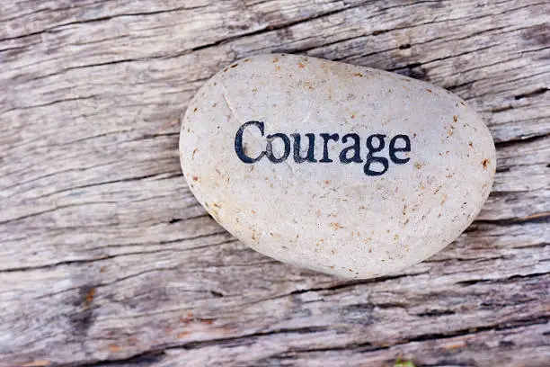Photo of The word courage written on a smooth white rock on wood