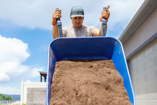 Western USA Home Improvement Young Adult Hispanic Male Mexican American Homeowner Landscaping Yard Shoveling and Moving Top Soil in a Wheelbarrow Photo Series with Matching 4K Video Available