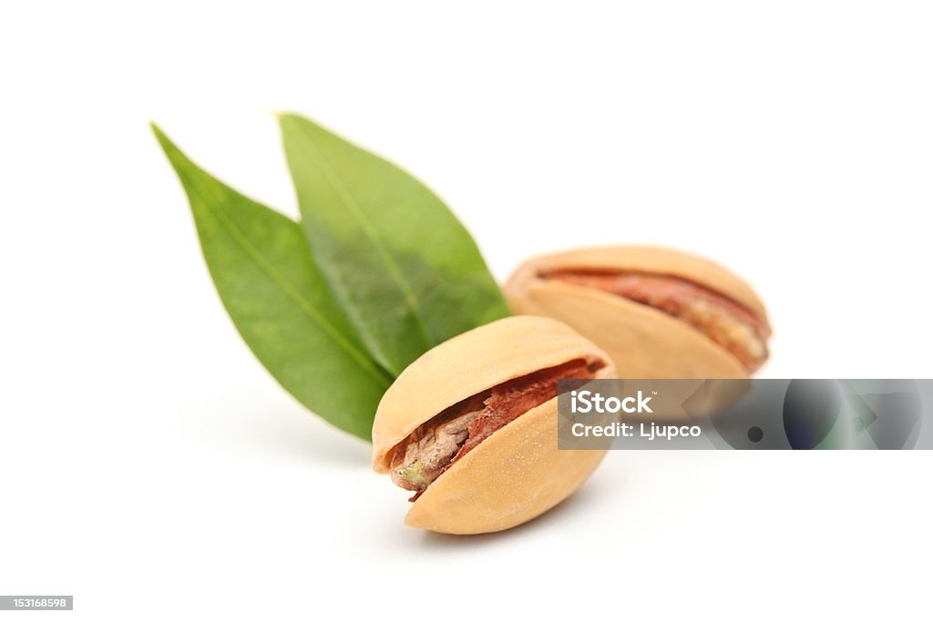 Two salted and roasted pistachio nuts Two salted and roasted pistachio nuts with shell and green leaves isolated on white background Appetizer Stock Photo