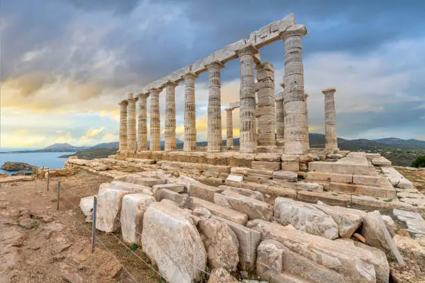 View of the ancient 5th-century BCE Temple of Poseidon and Aegean Sea under dramatic autumn skies at Cape Sounion, near Athens, Greece.