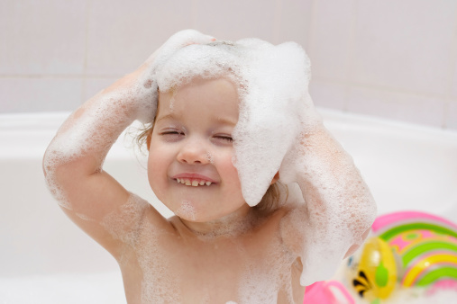 Cute baby is washing her hair in bath 