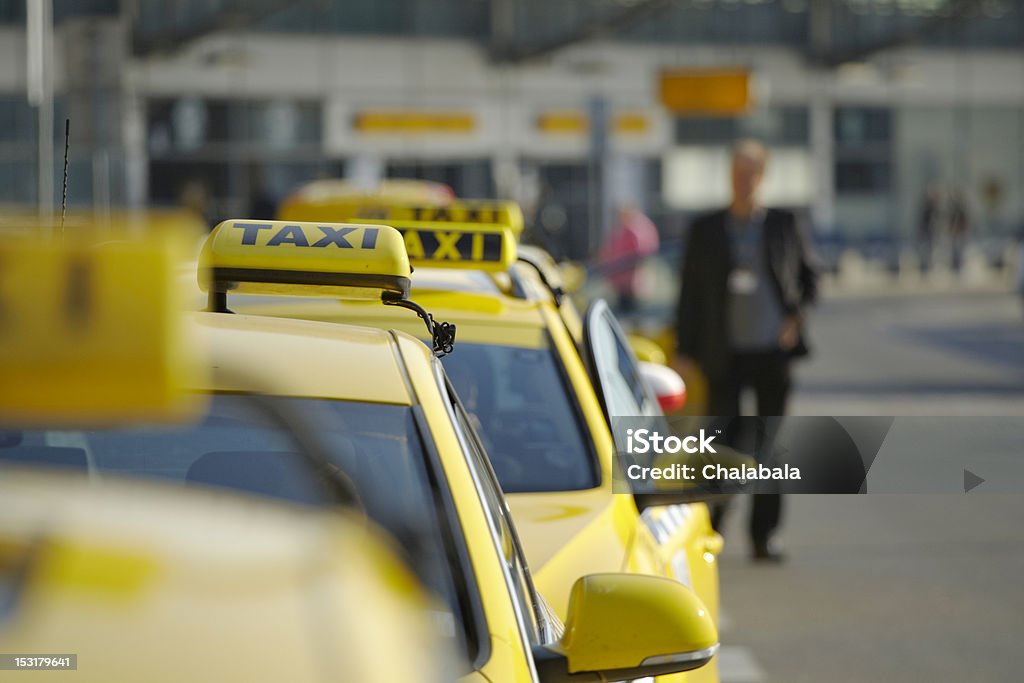 A line of taxis and an out of focus man Taxi car are waiting in row in front of the terminal Prague Airport. Taxi Stock Photo