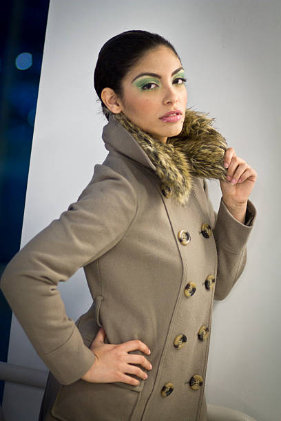 A beautiful Hispanic woman in a tan winter coat with green eyeshadow and pink lips.