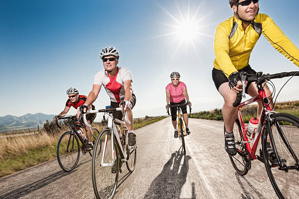 Road Cyclists Riding Together A small group of four road cyclists rides down an empty rural road with the sun at their backs for exercise and fun. racing bicycle photos stock pictures, royalty-free photos & images