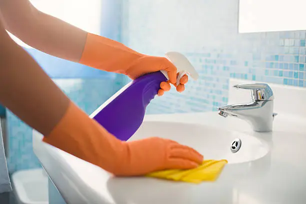 woman doing chores in bathroom at home, cleaning sink and faucet with spray detergent. Cropped view