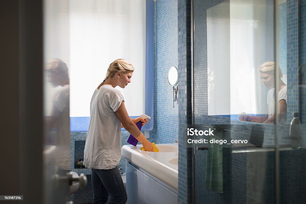 Young woman doing chores and cleaning bathroom at home Housework and domestic lifestyle: woman doing chores in bathroom at home, cleaning wash basin and tap with spray detergent Housekeeping Staff Stock Photo