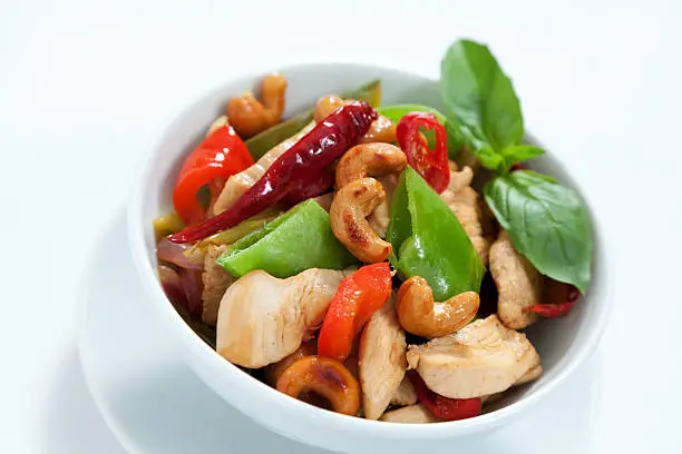 Chicken with cashew nuts, chili, capsicum and snow peas on a white background