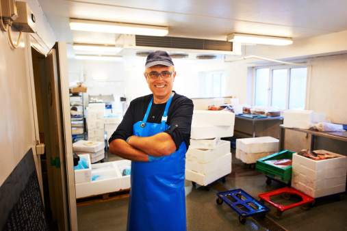 Portrait of a happy mature male fishmonger standing in his workroom with arms crossed