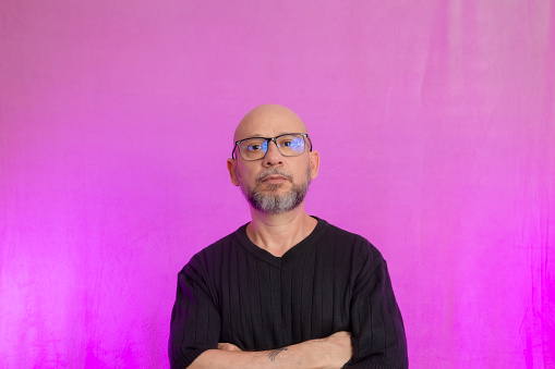 Portrait of a serious 50-year-old man with a beard and bald head. Isolated on pink background.