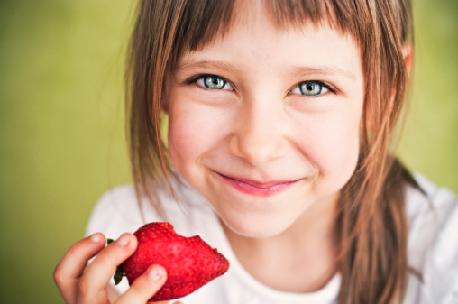 Smiling little girl holding a bitten strawberry