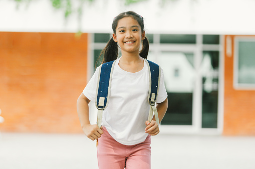 Portrait of a smiling little asian girl with backpack at school