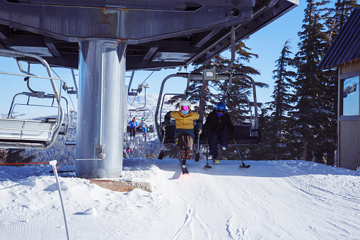 Two adult adaptive athletes exit the ski lift at the top of the mountain.