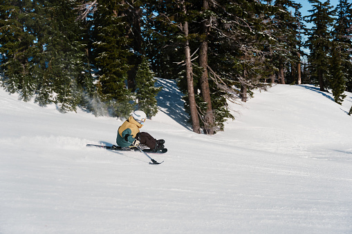 Profile view of an adaptive athlete riding down the mountain using a mono ski sit-ski.