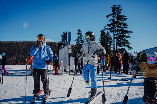 A group of friends, some of which are adaptive athletes, gather together and talk outside a ski lodge between ski runs on a beautiful and sunny winter day.