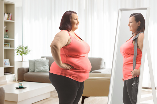 Corpulent woman looking at a slimmer version of herself in the mirror at home