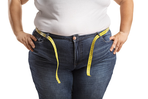 Overweight female body in jeans with measuring tape around waist isolated on white background