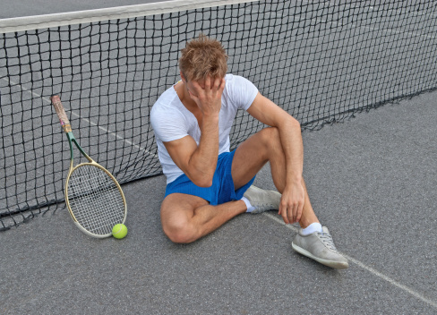 Disappointed tennis player, sitting on the ground, holding his head.