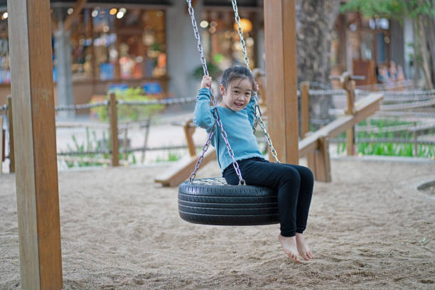 Little girl smiling while playing on a swing set in playground joyfully, side view