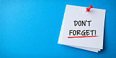 White Sticky Note With Don't Forget And Red Push Pin On Blue Cardboard Background