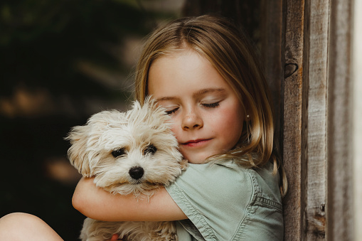 A close up image of a beautiful little girl, eight years old, smiling as she snuggles with her puppy.