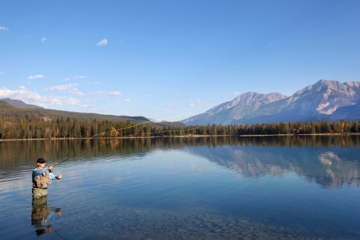 Fisherman fly fishing in Lake Edith with Rocky Mountains and blue skies in the background.