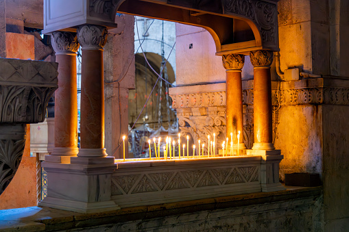 Burning votive candles with lit flames, also known as prayer candles, inside the Church of the Holy Sepulchre in the Old City of Jerusalem, Israel.