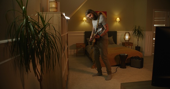 Man plays guitar in bedroom.