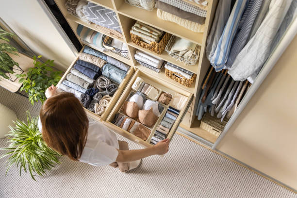 eine junge frau wählt aus, welchen bh sie tragen möchte, während sie vor einem ordentlich arrangierten kleiderschrank steht. das konzept der unterwäscheaufbewahrung und raumorganisation. - neat stock-fotos und bilder