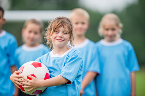 A small group of school aged children stand together as they pose for a portrait after a soccer game.  They are each wearing a blue jersey and are smiling as they enjoy the fresh air.