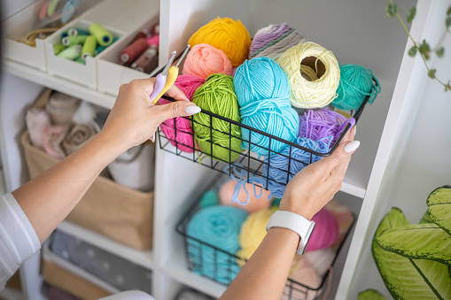 Female hands placing basket with colored ball of yarn for art crochet knitting ribbon cotton wool thread for hobby. Woman tailor sewing materials comfortable storage cupboard arrangement organize