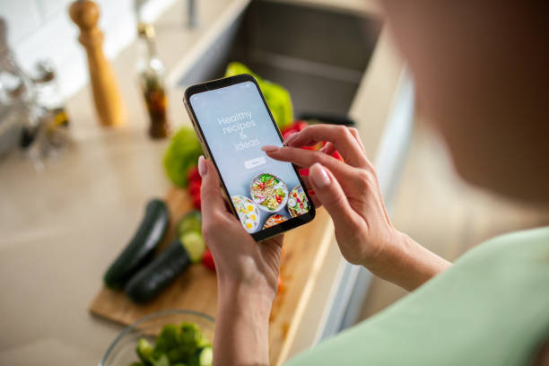 istock Young woman using a diet app on her phone while preparing a healthy food dish at home 1532305849