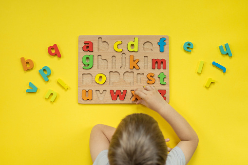 Childish hands holding alphabet wooden board with colored font letters in cells closeup isolated on white. Boy girl kid arms intellect game playing early development primary education letters learning