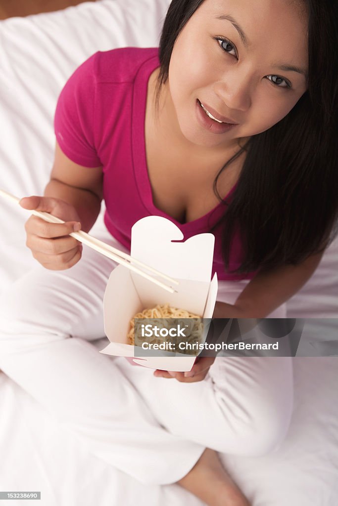 Joven mujer asiática comiendo comida china en la cama - Foto de stock de 20-24 años libre de derechos