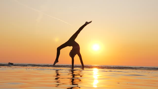 Beautiful shot of young gymnast girl against golden sunset at sea beach