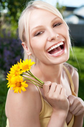 Cute smiling little girl, in a blue dress, holds a bouquet of daisies, stands in a field with daisies on a sunny day. Copy space