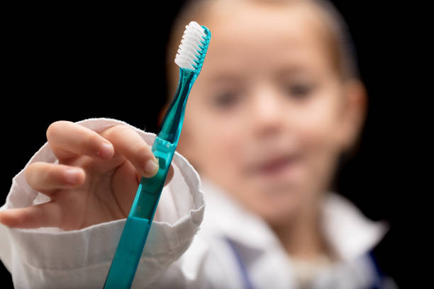Brush your teeth! says the little girl dentist. A small, blurred girl in an oversized coat plays dentist, showcasing a toothbrush (in focus) urging you to brush for your health and to avoid bad breath
