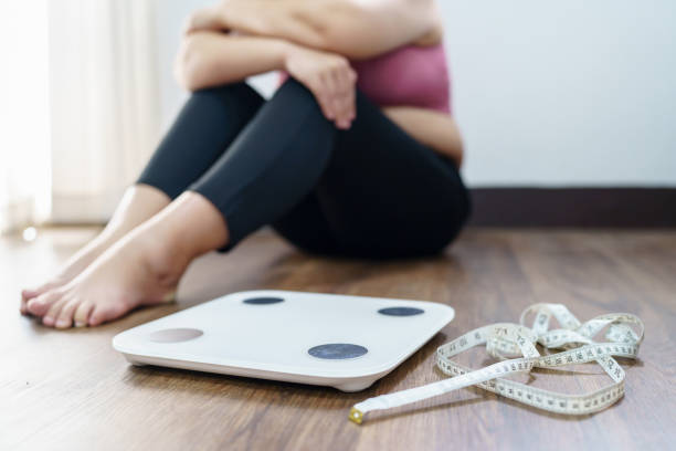 obese woman with fat upset bored of dieting weight loss failâ  fat diet and scale sad asian woman on weight scale at home weight control - dieting overweight weight scale healthcare and medicine imagens e fotografias de stock