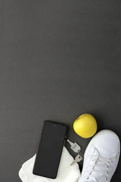 Photo of Objects to exercise on a mat with cell phone, apple, bottle of water, headphones, tennis towel and watch