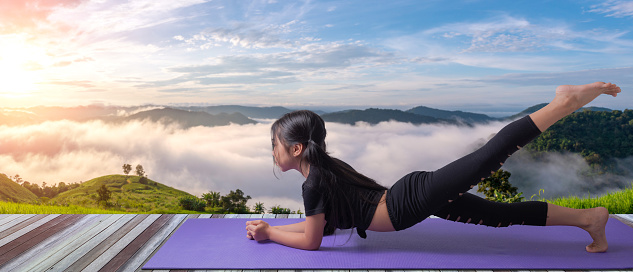 Mid Adult Asian/ Indian Woman performing Yoga asana or meditation in tree position at garden on yoga mat. Concept of healthy lifestyle.