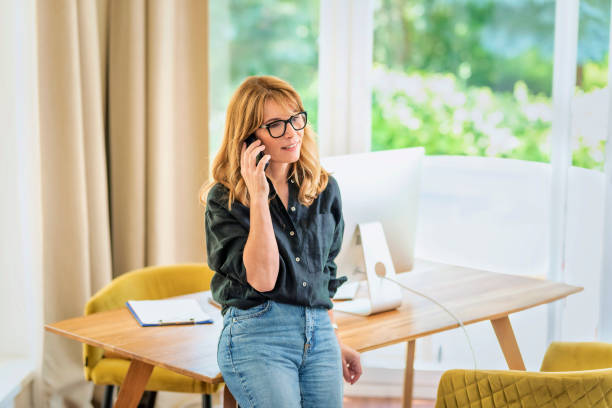 istock Mid aged woman standing at desk and using cellphone 1532589786