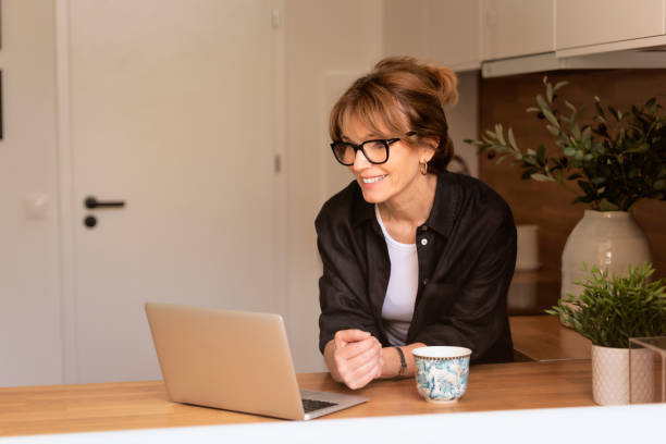 istock Mid aged woman standing at the kitchen at home and using laptop 1532590302