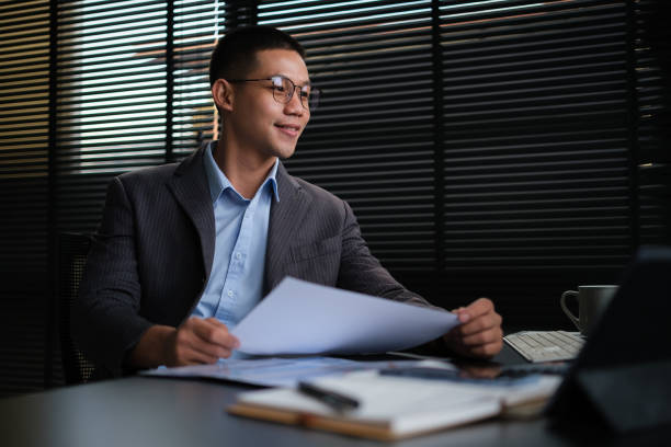 empresario asiático analizando informes financieros y usando computadora portátil en la oficina. - dirigir una empresa familiar exitosa fotografías e imágenes de stock