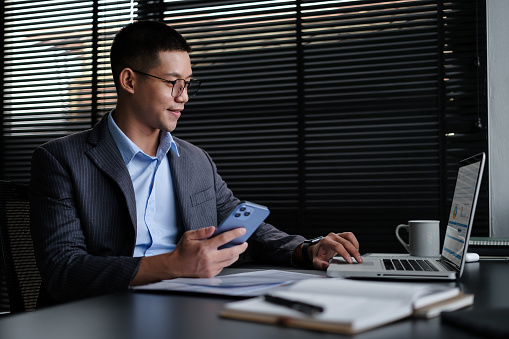 Young businessman using laptop and doing some paperwork at his personal office.