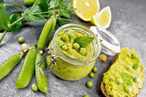 Hummus from green peas and chickpeas in a jar, pea pods, lemon and sandwich on granite countertop background