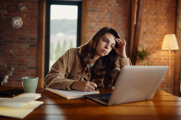 istock Bored creative woman taking notes while working on laptop at home office. 1532649536