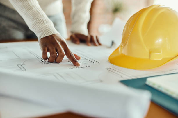 Close up of black architect examining blueprints in the office. Close up of unrecognizable African American building contractor working on blueprints in the office. african american architecture stock pictures, royalty-free photos & images