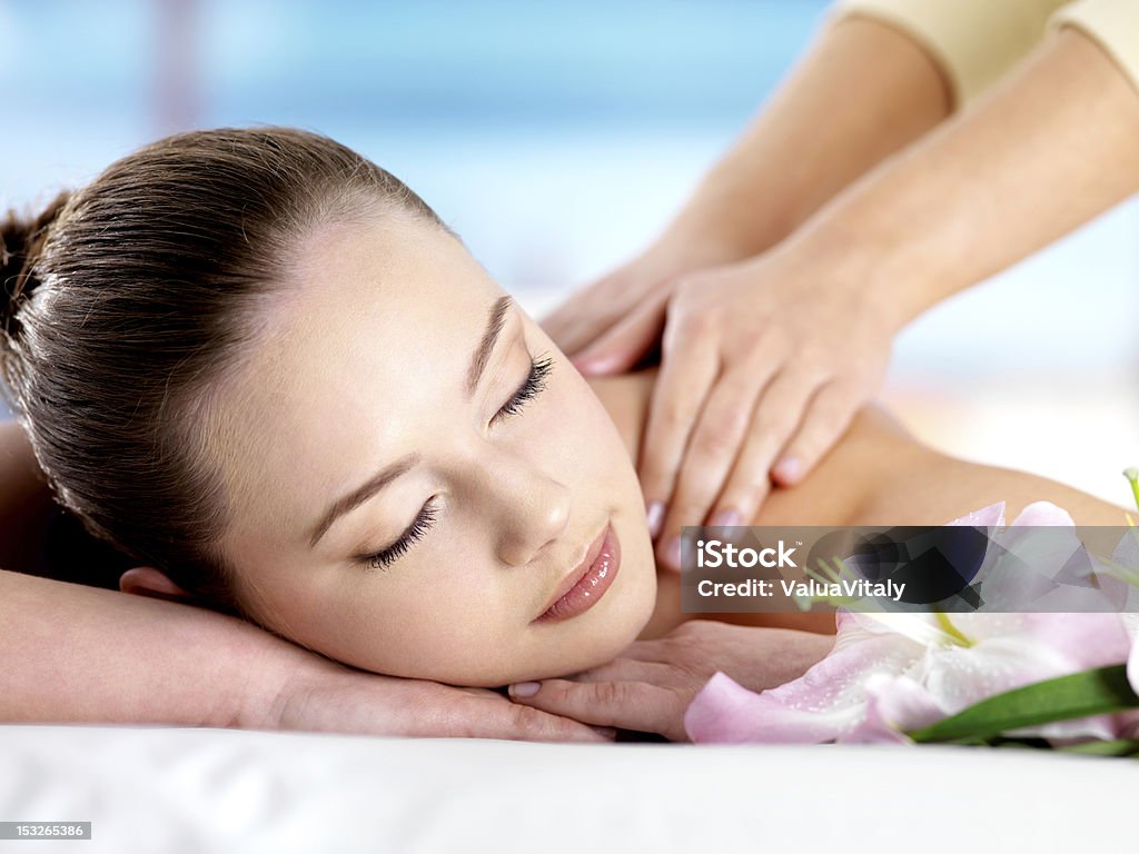 Woman having massaging Beautiful young woman with attractive face having a massage for  shoulder on resort - colored background Adult Stock Photo