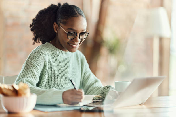 istock Happy black creative woman taking notes while working on laptop at home office. 1532659620