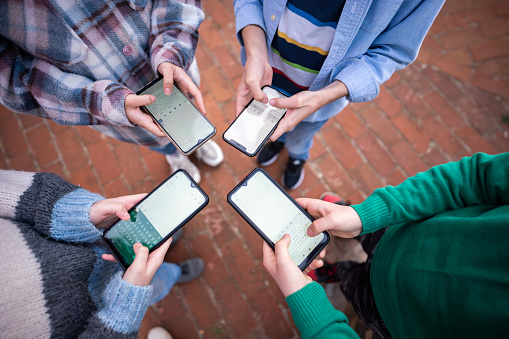 High angle view of unrecognizable teens in circle holding smart mobile phones and writing a message